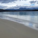 Wide-angle view of Planter Beach near Cockle Creek, Tasmania, showing a long stretch of shoreline under a moody, threatening sky with rugged mountains