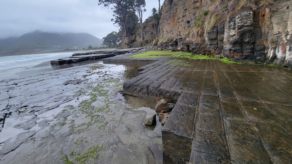 A coastal view of the Tessellated Pavement at Eaglehawk Neck, Tasmania, featuring the natural geometric rock fractures creating leading lines towards other rock formations