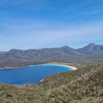 The iconic Wineglass Bay lookout view on Tasmania's East Coast, showing the white sand beach and azure ocean during a sunny day on the Great Eastern Drive.